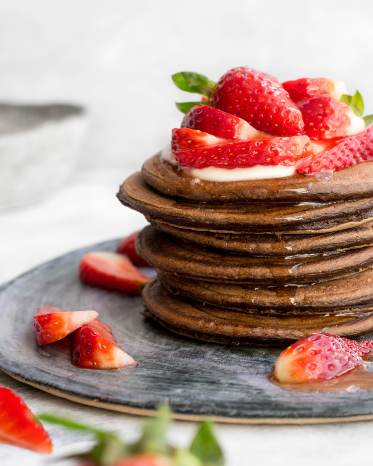 Cocoa pancakes served with yogurt, fresh strawberries and honey on a blue plate.