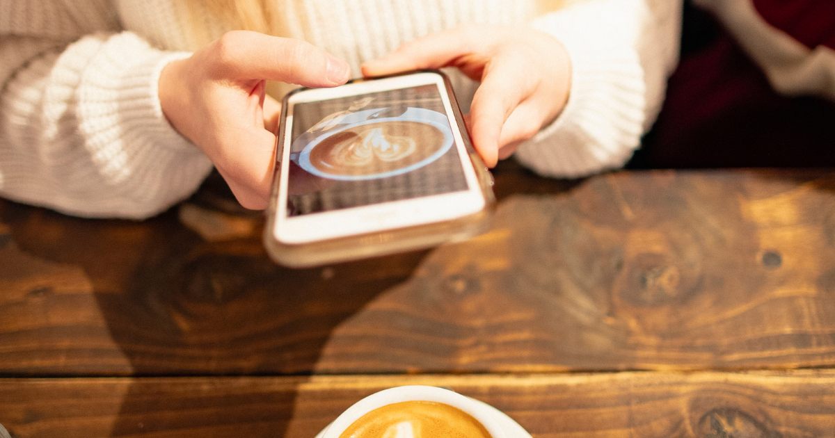 Woman holding a smartphone to take a social media photo of her coffee on a rustic wooden table