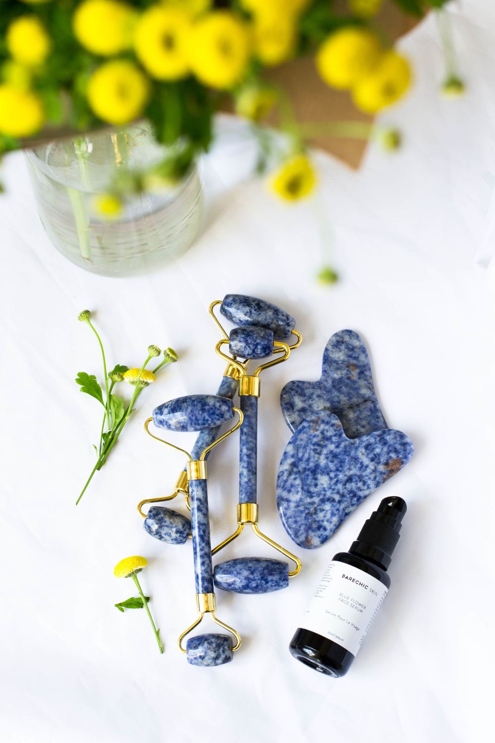 Lifestyle photo of gua sha tools and oil for facial treatments and yellow flowers.