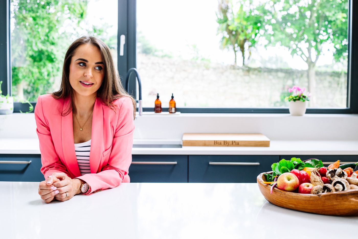 Woman wearing a pink blazer standing in a kitchen. Brand photography by Chiara Gianelli