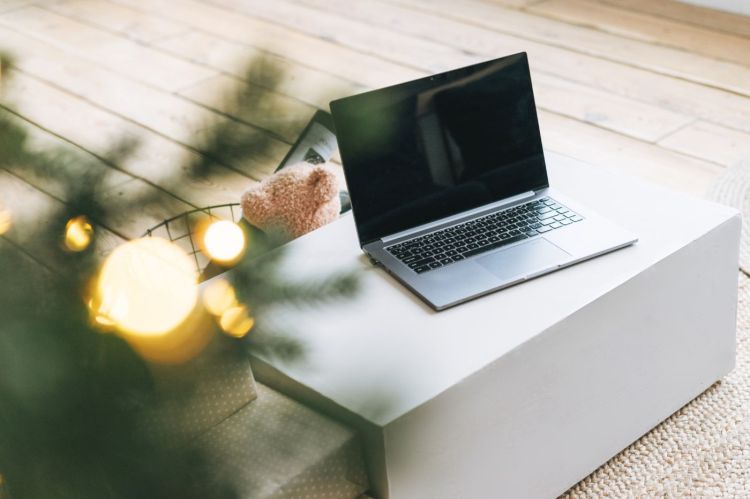 Decorative photo of a laptop with Christmas lights and a part of a Christmas tree in a corner of the image