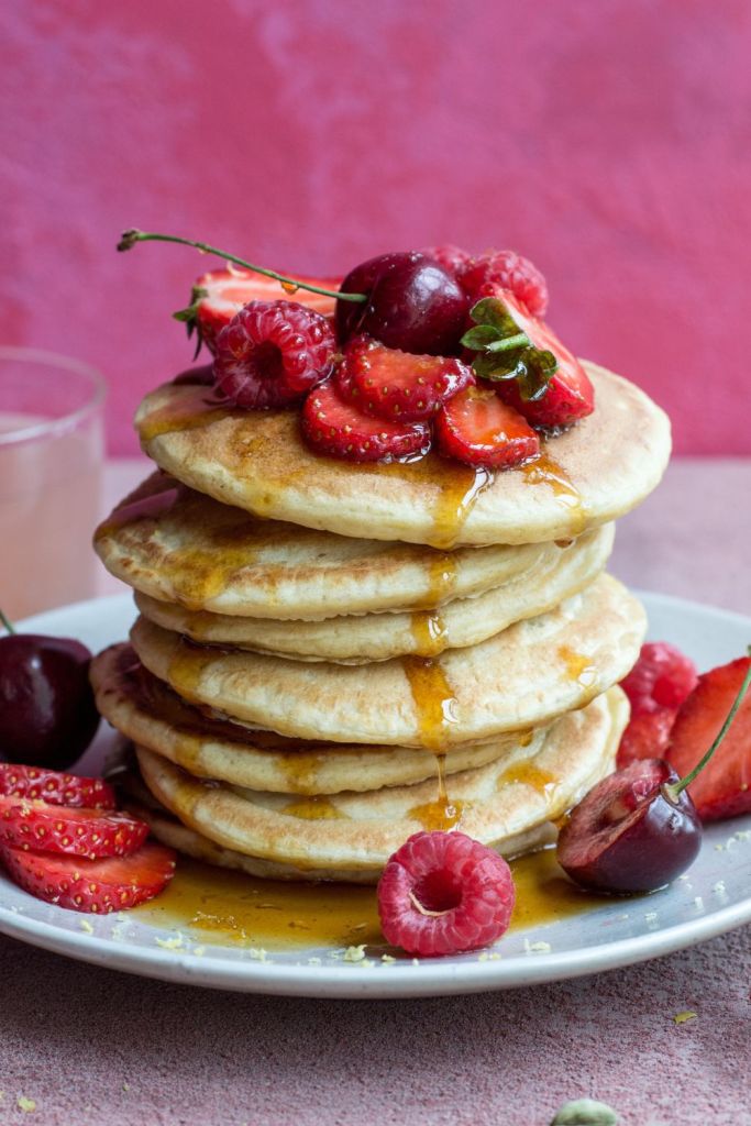 Stack of pancakes with berries, cherries and maple syrup. Styled on a pink background by Dublin food photographer Chiara Gianelli