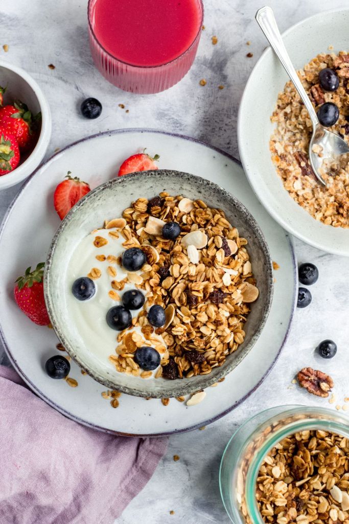 Bowls with granola, yogurt and berries on a marble background with a glass of pink smoothie. Styled by food photographer Chiara Gianelli