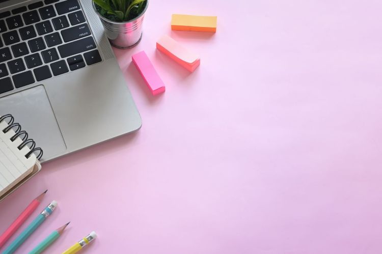 Decorative lifestyle photo of a purple desk with a laptop, sticky notes, a small plant, a notebook and pencils