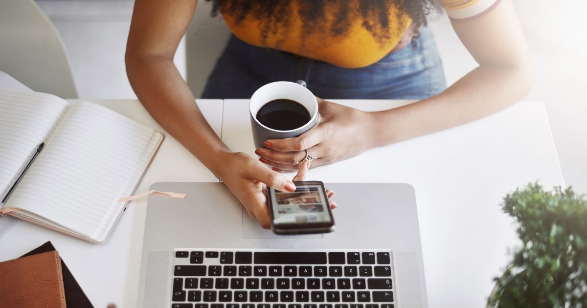 Decorative image featuring a woman scrolling on her smartphone and holding a cup of coffee at the desk with an open laptop and notebook