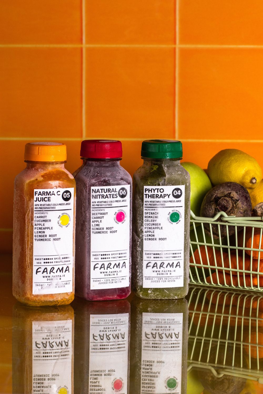 Three bottles of frozen cold pressed juices of different colours (orange, dark purple, green) placed in front of a background made of orange tiles. Product photography by Chiara Gianelli