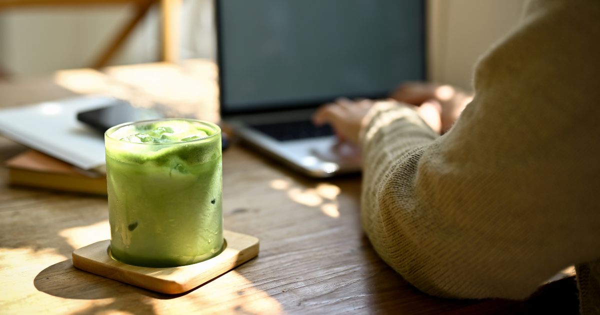 Decorative photo of a person working on a laptop with a glass of matcha beside it